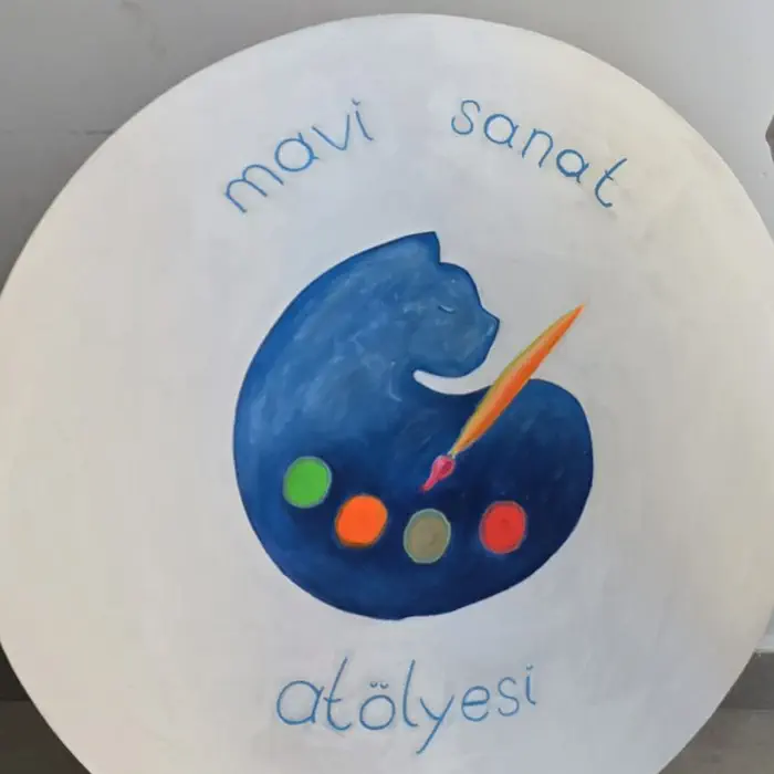 Atölyenin el boyaması yuvarlak tabelası: mavi kedi, palet ve turuncu fırça